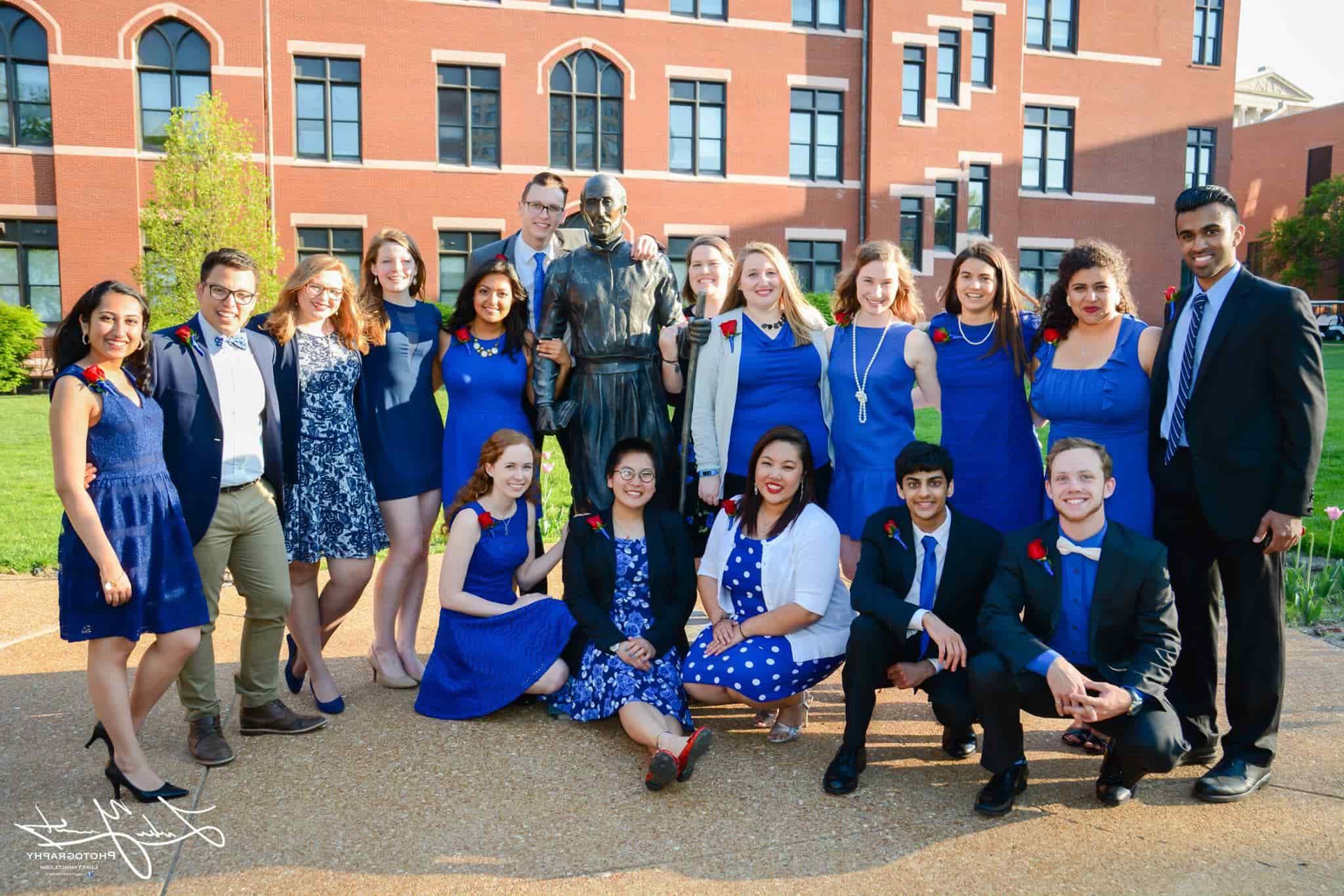 A group of students pose for a photo outside with a campus building in the background.