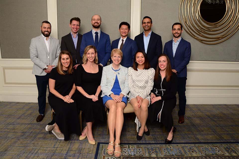 A group of alumni pose for a photo with the dean in a ballroom.