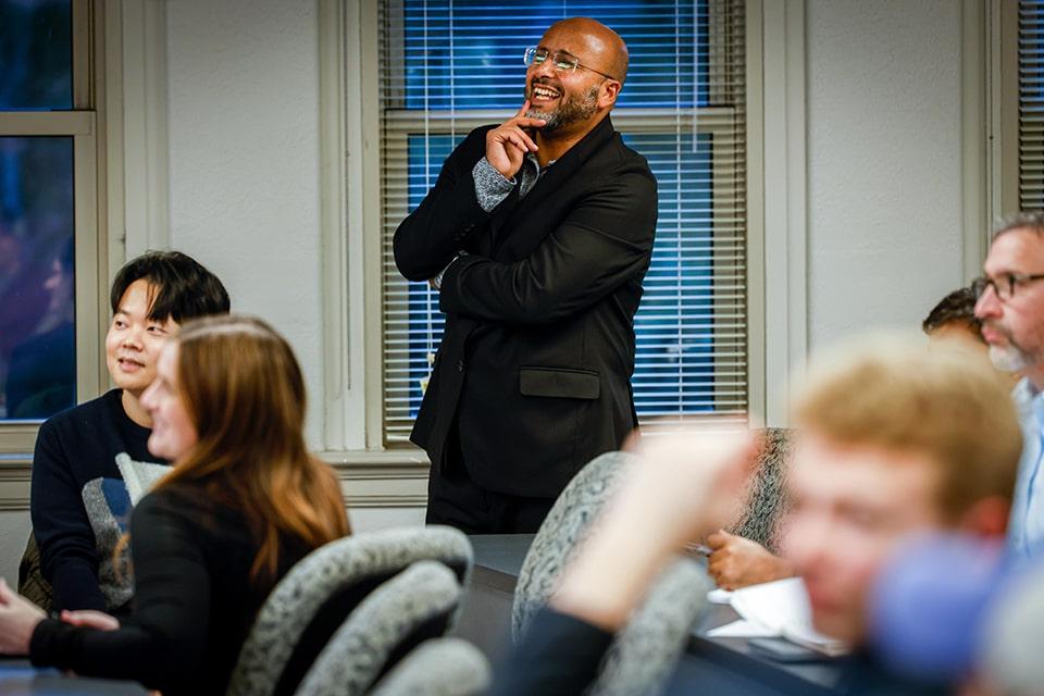 A seminar leader stands in a classroom and smiles.