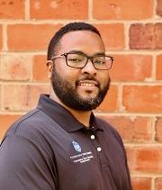 Michael Hankins, headshot, wears a 博彩网址大全 polo shirt and smiles, standing in front of a brick wall.