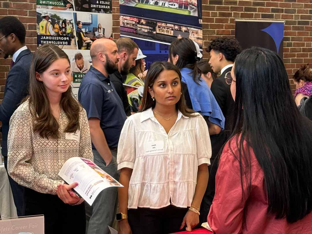 Two students talk to an employer in a room filled with people.